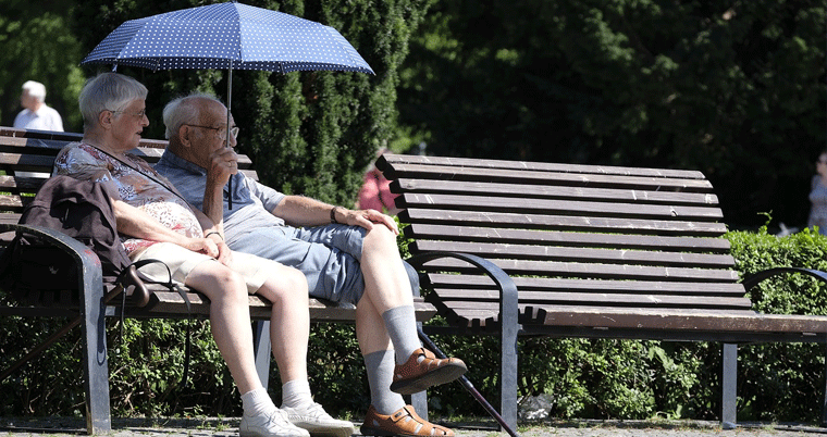 Rentner Ehepaar mit Regenschirm auf Parkbank