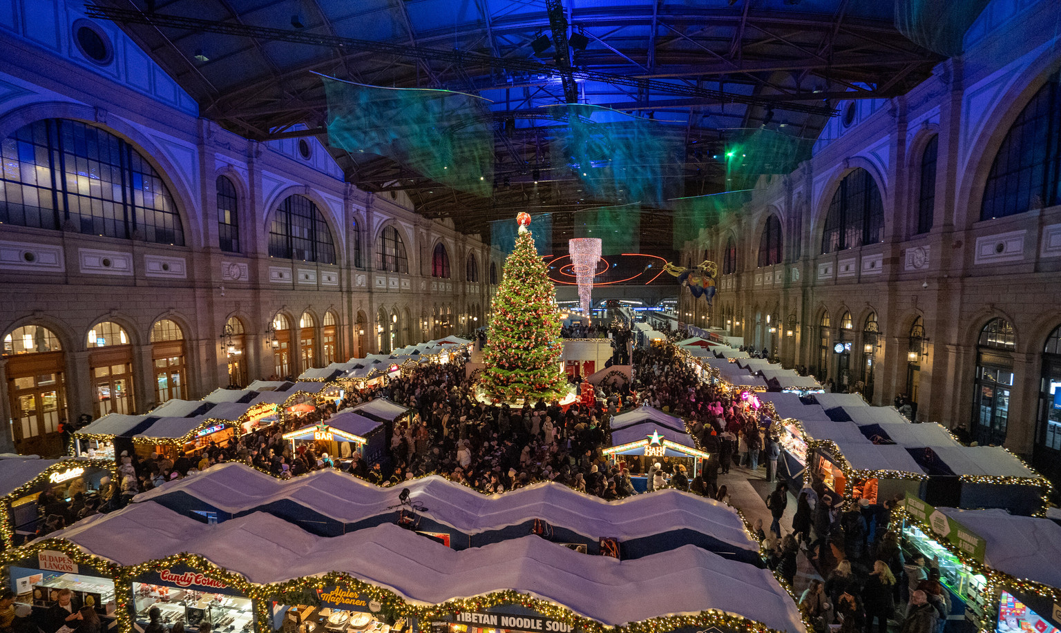 Polarzauber in der Bahnhofshalle Zürich, Saison 2025: Reihen von Markthäusern unter dem Hallendach, in der Mitte der Weihnachtsbaum